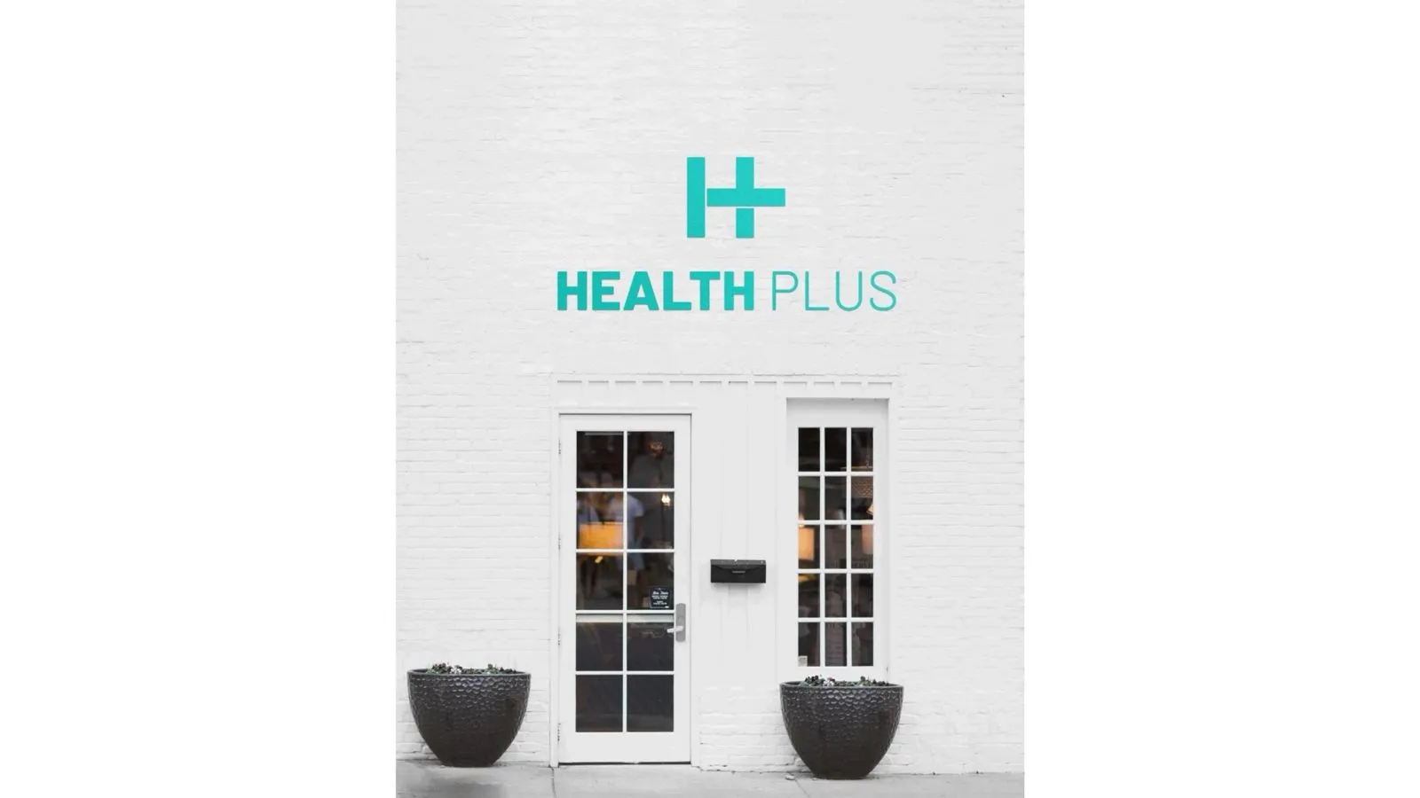 White brick storefront with a teal Health Plus sign and logo above double doors, flanked by two large round planters at the entrance
