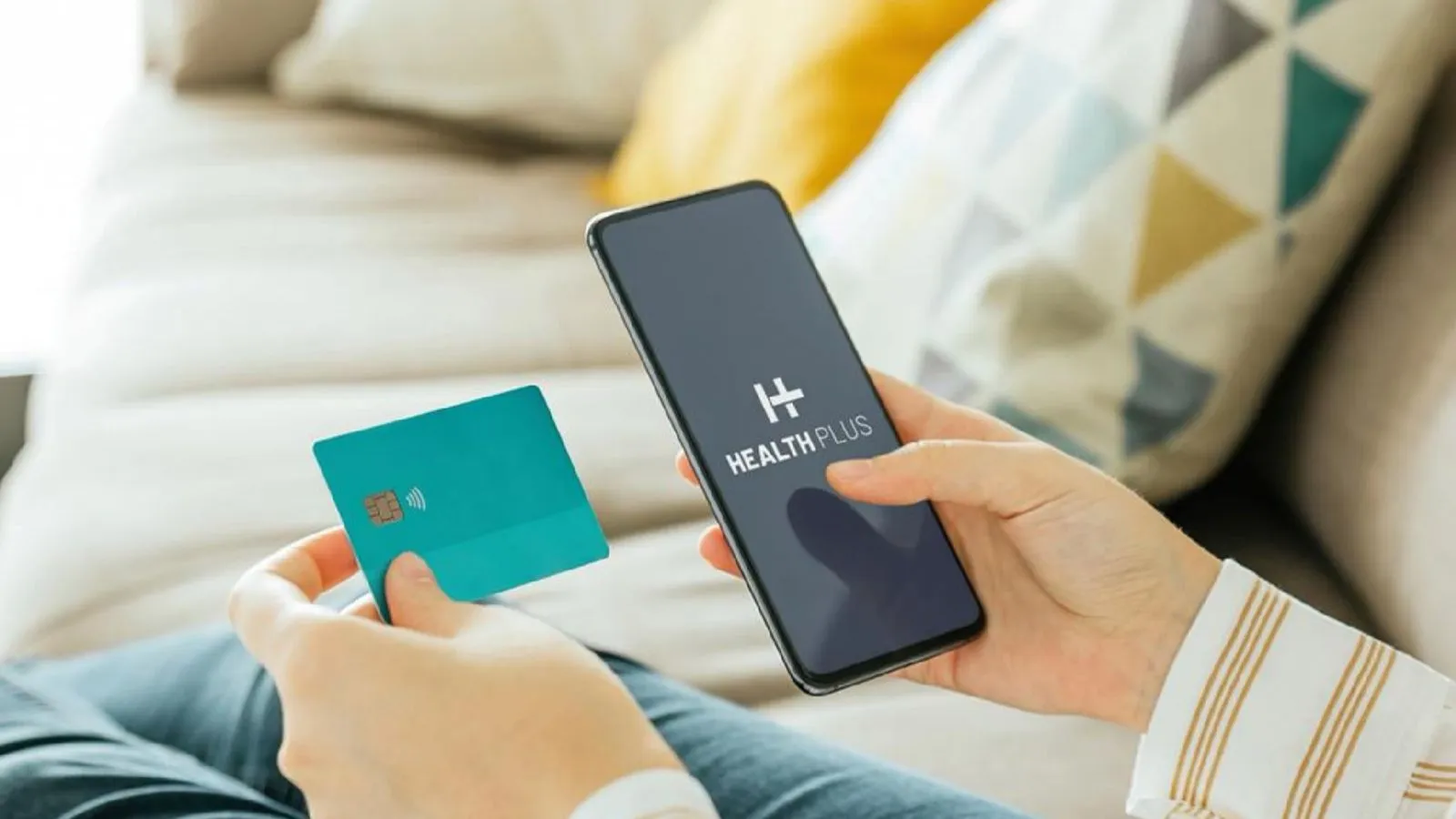 Person holding a teal credit card in one hand and a smartphone displaying the HealthPlus app in the other.