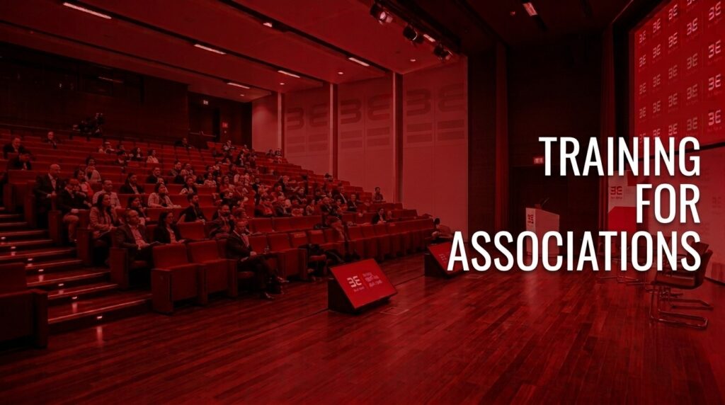 Audience seated in a lecture hall with a stage on the right, overlaid by bold white text: 'Training for Associations'.