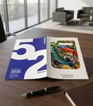 Two brochures on a desk near a window, one with a large blue number 5 and the other with a colorful map image, with a black pen in front.