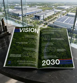 Open magazine on a black table showing a 'VISION 2030' spread with green graphics, viewed through large office windows at a cityscape edge.